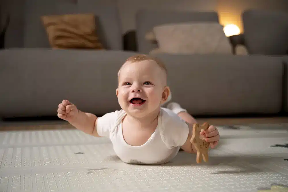 Um bebê alegre fazendo tummy time num tapete, uma atividades no método Montessori recomendadas.