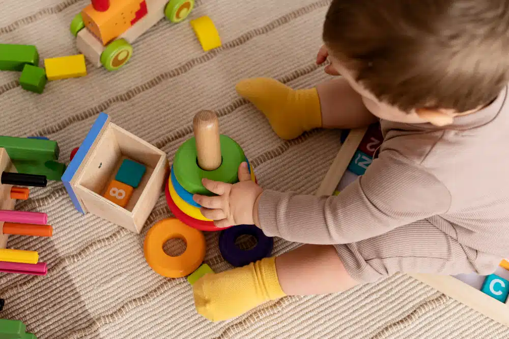 Um bebê sentado no chão brincando com brinquedos de madeira, método Montessori.