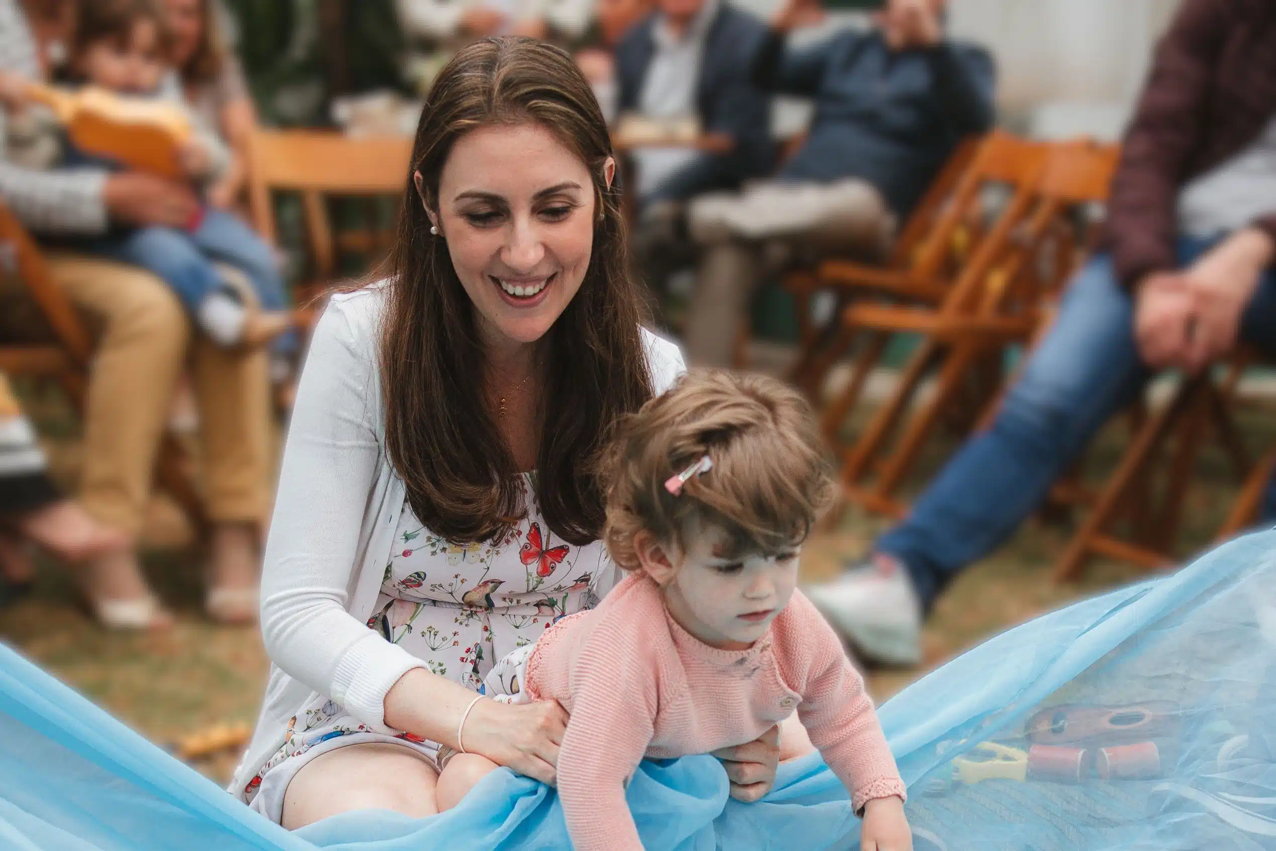 Uma mãe com a filha brincando na grama com um grande véu azul simulando o mar, fazendo refletir o quão brincar é urgente.